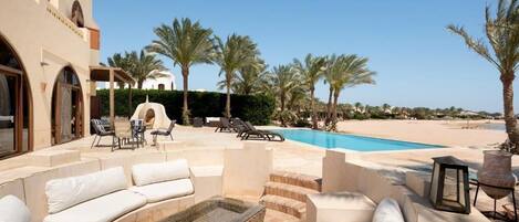 A poolside area with outdoor seating, palm trees, and a clear view of the beach.