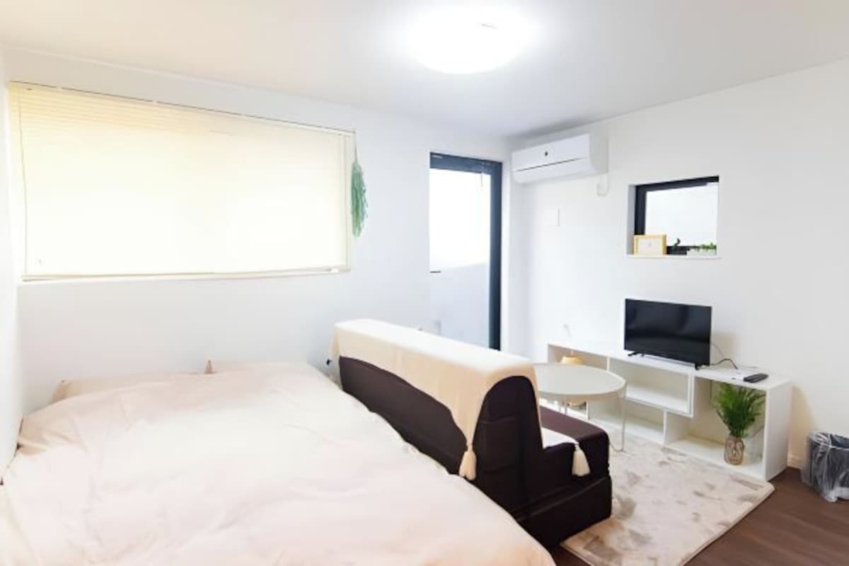 Et moderne hotelværelse med seng, lille sofa, fjernsyn og skrivebord.