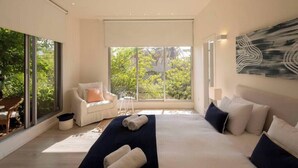 Une chambre moderne avec un grand lit, un canapé et une vue sur la verdure grâce à de grandes fenêtres.