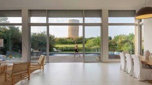 Une pièce spacieuse avec de grandes fenêtres, un coin repas et une vue sur un jardin et un grand bâtiment à l’extérieur.