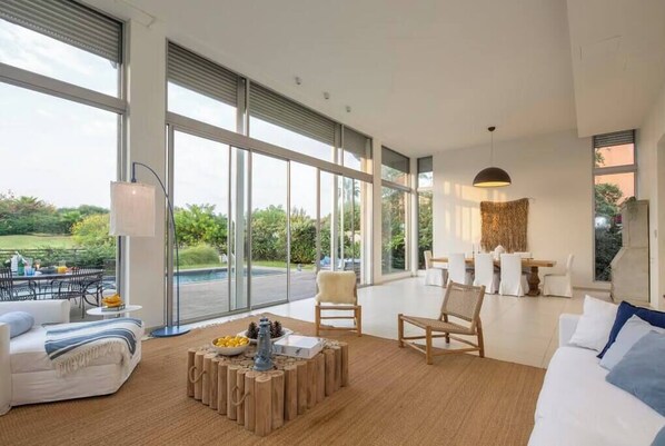A spacious living room with large windows, a dining area, and a view of the outdoors.