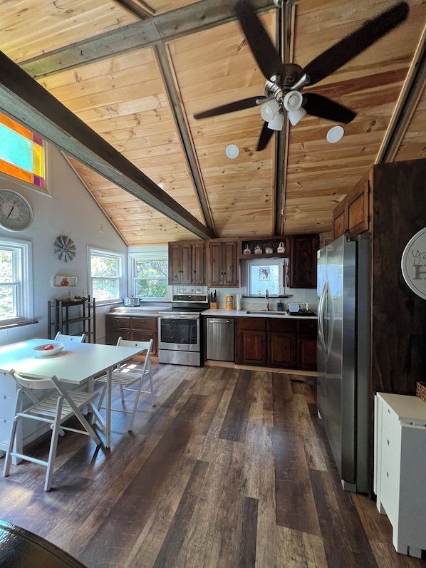 A kitchen with wooden cabinets, stainless steel appliances, a dining area with a white table and chairs, and a ceiling fan.