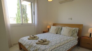 A neatly made bed with a patterned bedspread, two bedside lamps, and a window with curtains. - G3 Polis Gardens - includes WiFi & A/C  (Polis)