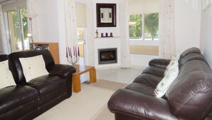 A living room with two leather sofas, a wooden coffee table, a fireplace, and a large window with curtains. - G3 Polis Gardens - includes WiFi & A/C  (Polis)
