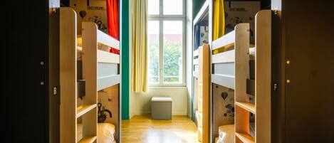 A corridor with bunk beds on either side, a window at the end, and a bench in the center.