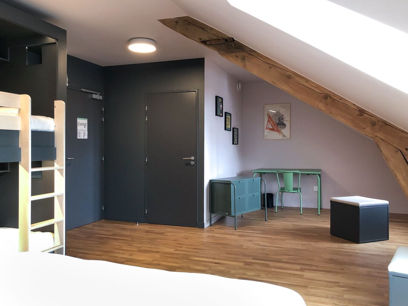 Una habitación con cama litera, un escritorio con sillas, un radiador y una puerta.