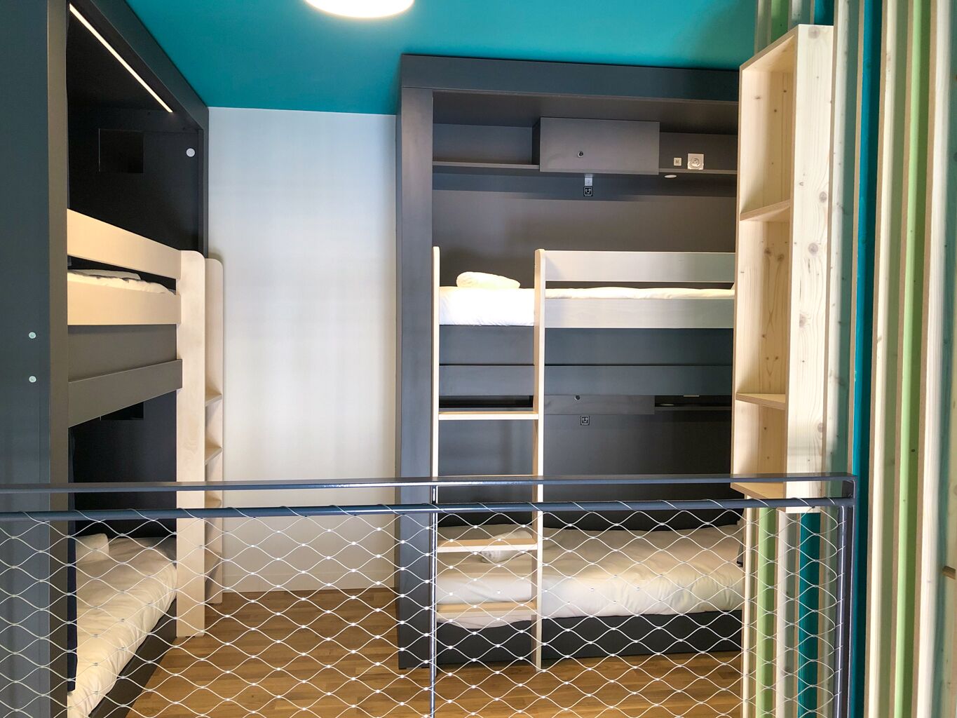 A bunk bed room with a wooden floor, a ceiling light, and a metal gate.