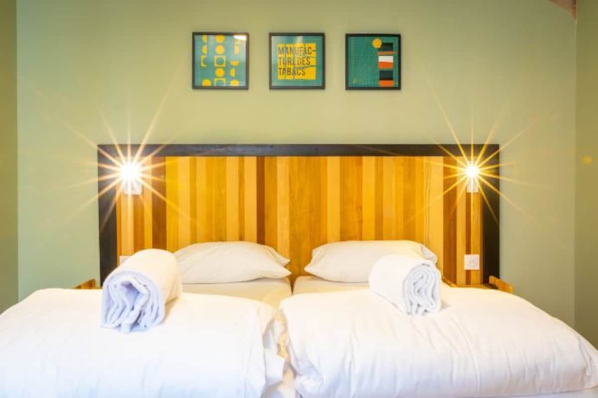 Ett hotellrum med två sängar, och på varje sänggavel ligger en hoprullad vit handduk. På väggen ovanför sängarna hänger tre inramade tavlor.