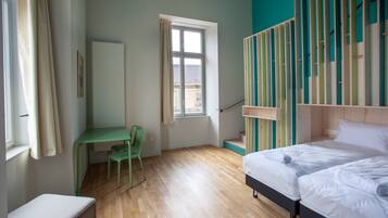 Une chambre à coucher avec un lit, un bureau et une chaise. Il y a une fenêtre et une vue sur l’extérieur.