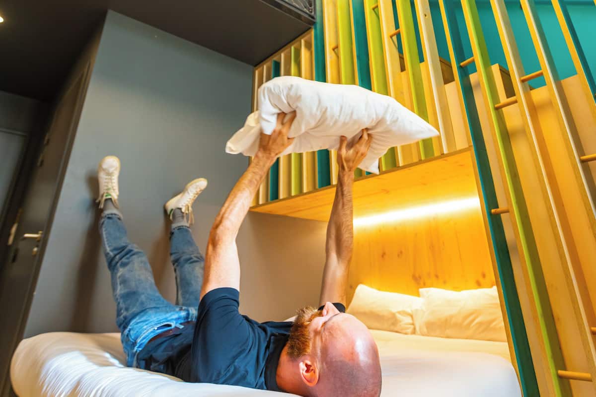 Ein Mann liegt in einem Zimmer auf einem Bett, über ihm befindet sich ein Etagenbett.