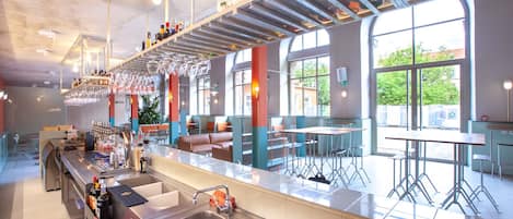 Un área de bar moderna con una barra larga, taburetes y un espacio de asientos con un sofá y mesas.
