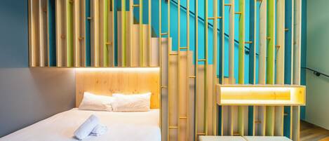 Une chambre d’hôtel moderne avec un lit parfaitement fait, une tête de lit en bois et un mur décoré d’un motif original en bambou.