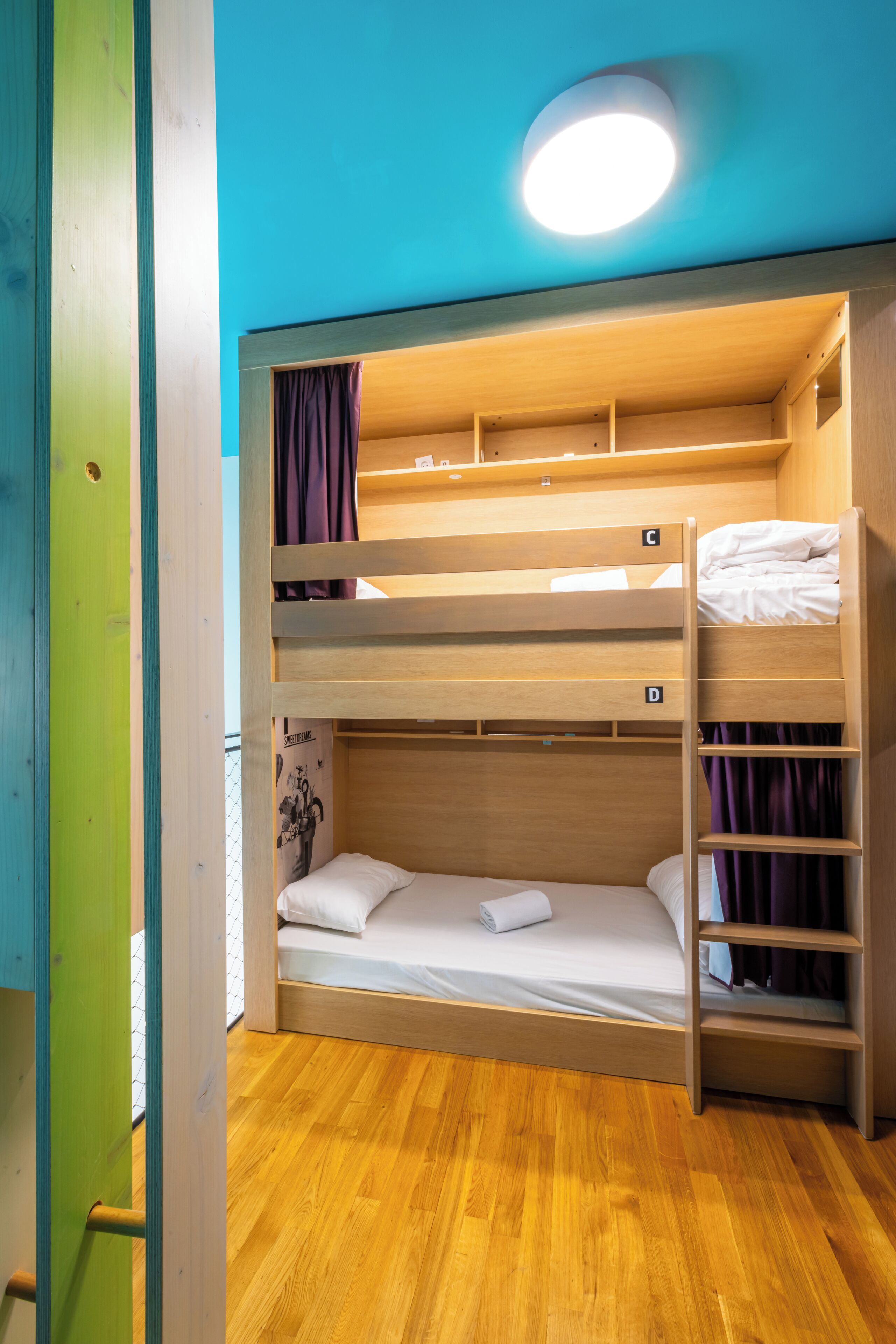 A bunk bed room with wooden bunk beds, a ladder, and a ceiling light.