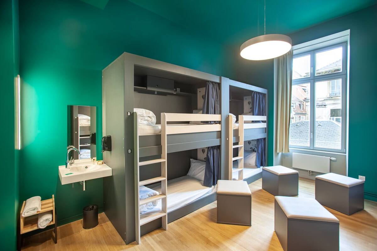 Ein modernes Zimmer mit Etagenbetten, einem Waschbecken, einem Spiegel und einem Fenster mit Blick auf Gebäude.
