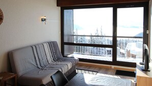 Ett mysigt vardagsrum med en soffa, en tv och ett stort fönster med utsikt över snötäckta träd.