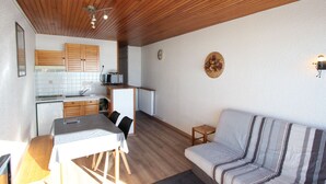 Ett kompakt bostadsutrymme med ett litet kök, ett matbord, en soffa och en liten pall.