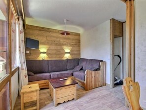 A cozy room with a wooden wall, a gray sofa, a wooden coffee table, and a TV mounted on the wall. - Beautiful renovated apartment for 4/5 in ski-in/ski-out location (Belle Plagne)