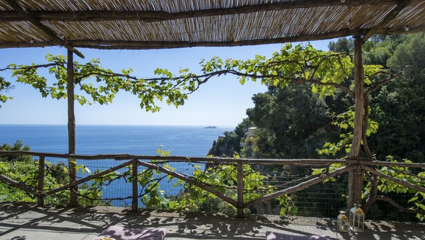 Eine Terrasse mit Meerblick, ein Tisch mit einem Glas und ein Hut.