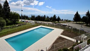 Une piscine rectangulaire dotée d’une terrasse carrelée, entourée d’une clôture et d’arbres, avec des montagnes en arrière-plan.