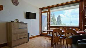Un salon comprenant un meuble en bois, un téléviseur et un coin repas avec des chaises et une table en bois.