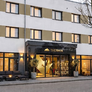 Een hotel met een moderne gevel, grote ramen en een opvallend 'Stay Wild Munich' bord.