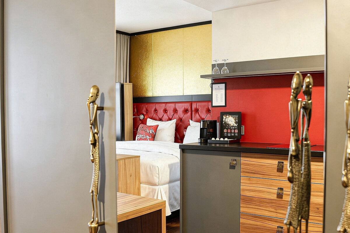 Una habitación de hotel con cama, kitchenette pequeña y pared de acento roja.