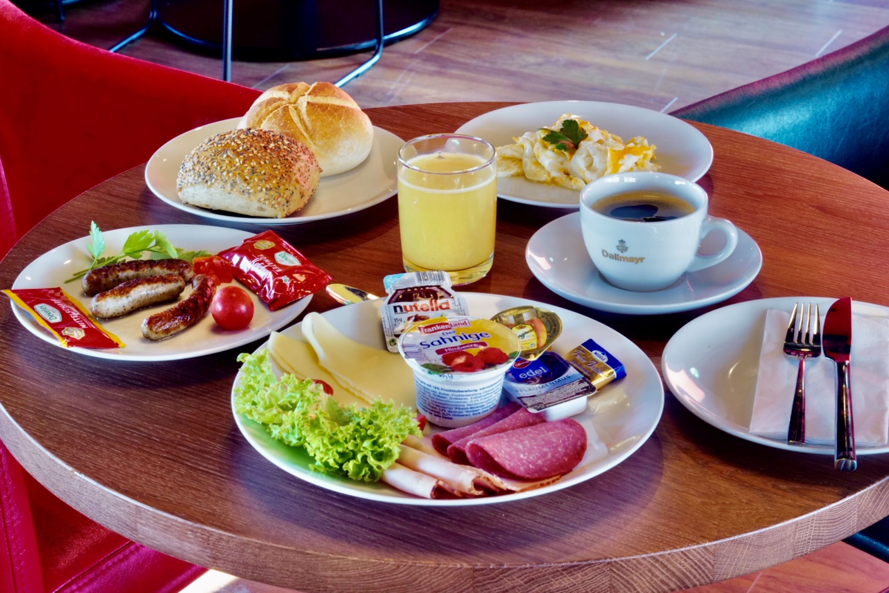 Ein gedeckter Frühstückstisch mit Speisen, darunter Würstchen, Brot, Eier und Kaffee.