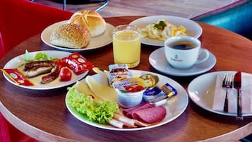 Ein gedeckter Frühstückstisch mit Speisen, darunter Würstchen, Brot, Eier und Kaffee.