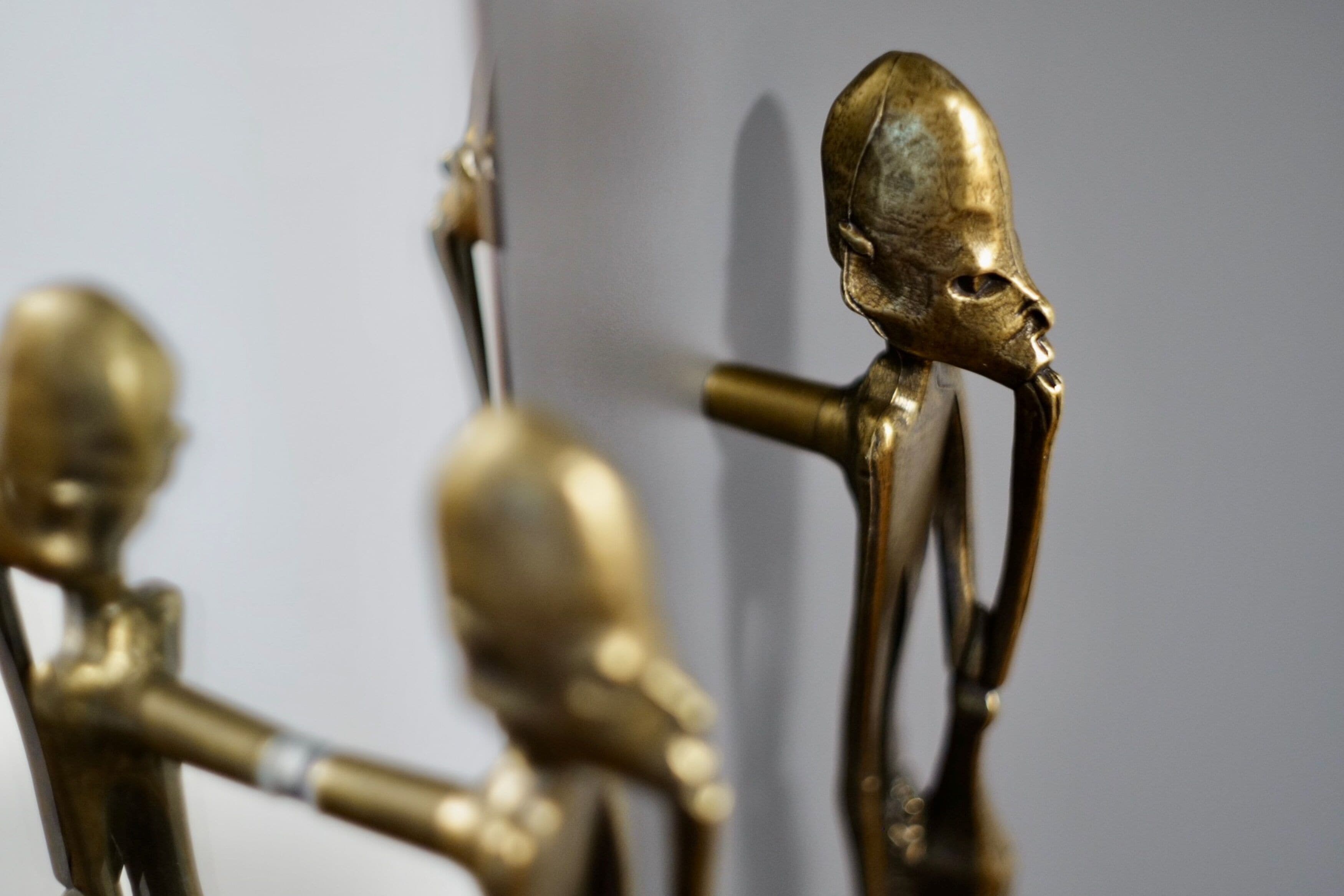 A close-up of a brass sculpture with a human figure and an elongated head.