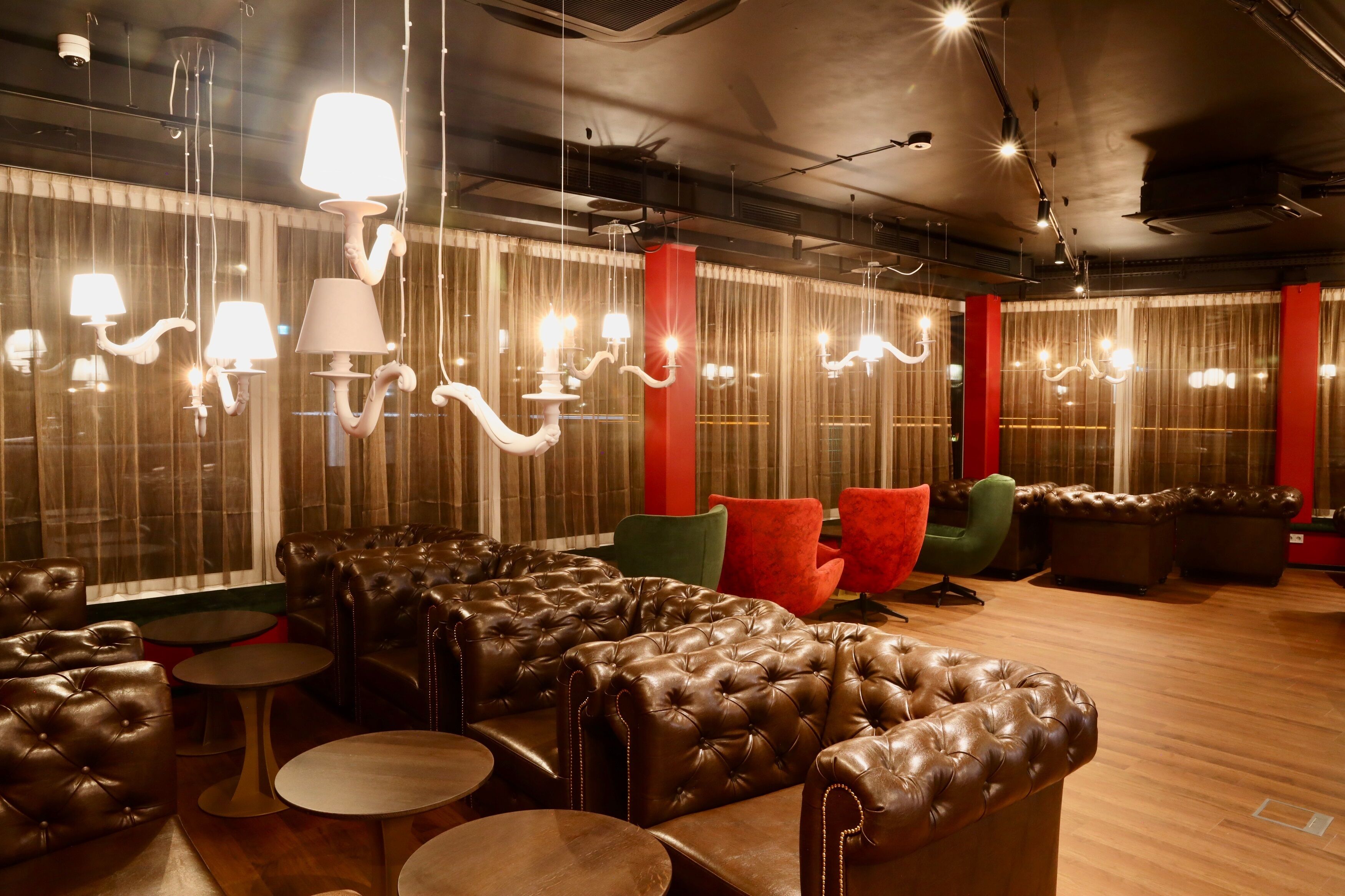A lounge area with leather sofas, red and green chairs, and hanging lamps.