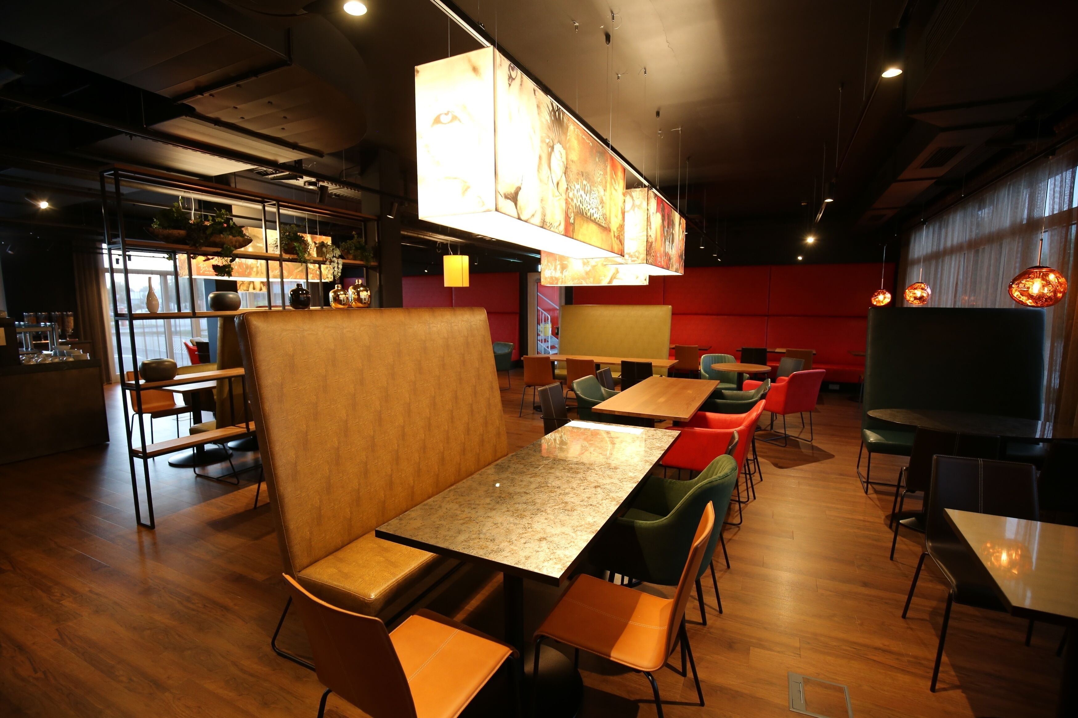 Un intérieur de restaurant moderne avec des tables et des chaises en bois, un bar et une grande œuvre d’art lumineuse accrochée au mur.