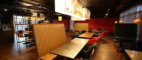 Ein modernes Restaurant-Interieur mit Holztischen und -stühlen, einer Bar und einem großen, beleuchteten Kunstwerk an der Wand.