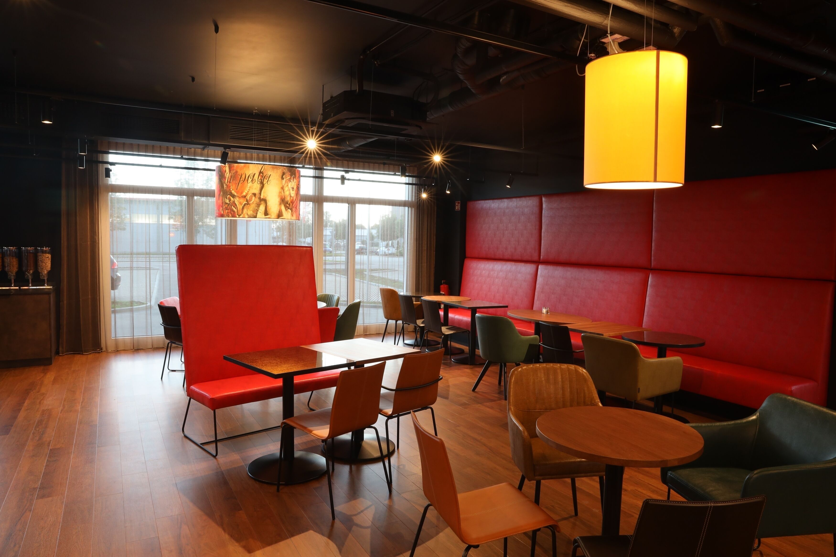 Een modern restaurant met rode banken, houten tafels en diverse zitmogelijkheden.