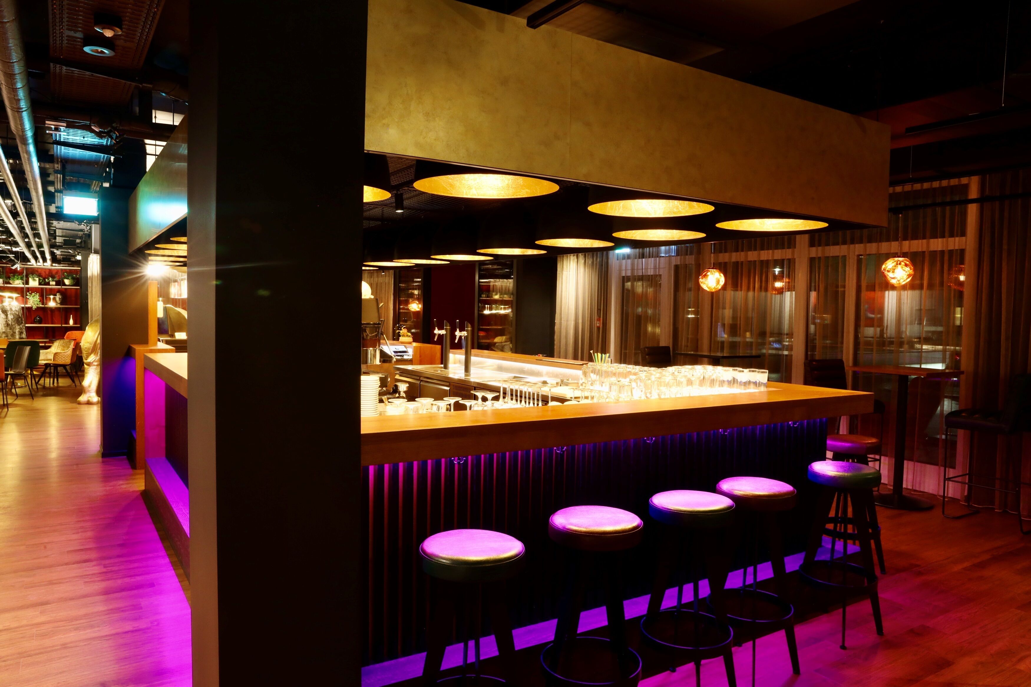 A bar area with a counter, stools, and pendant lighting.