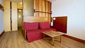 Ein kleines Zimmer mit einem hölzernen Bett, einem kleinen Tisch und einem Kleiderschrank.