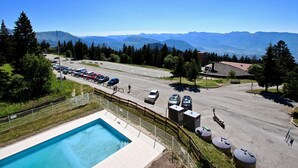 Ein Schwimmbad, ein Parkplatz und eine gebirgige Landschaft.