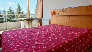 Ein Schlafzimmer mit einem hölzernen Kopfteil, einer roten floralen Bettdecke und einem Balkon mit Tisch und Stühlen.