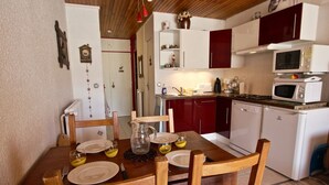 Une cuisine compacte avec des meubles blancs et rouges, une table à manger en bois avec des chaises, et un four à micro-ondes.