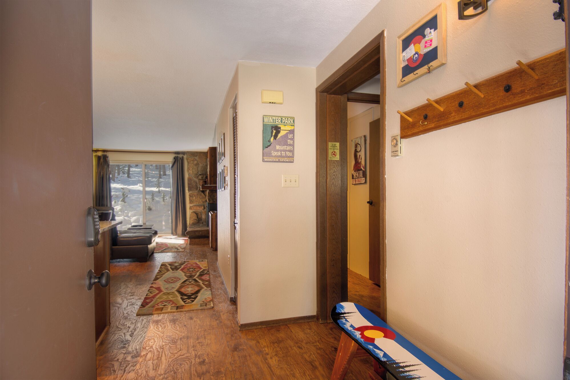 A hallway with a wooden floor, a rug, and a door with a coat rack.