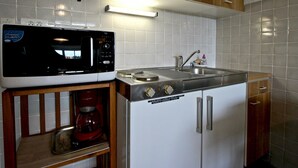 A compact kitchen with a microwave, sink, and wooden cabinets. - Bright studio with loggia near slopes and shops (Chamrousse)
