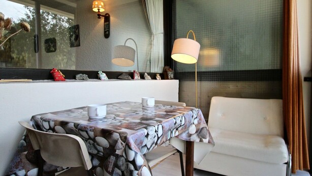 A dining area with a table covered in a pebble-patterned tablecloth, two chairs, a sofa, and a floor lamp. - Bright studio with loggia near slopes and shops (Chamrousse)