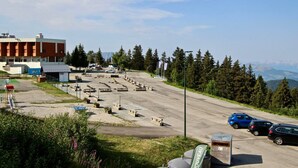 A parking area with several cars, a building with a red facade, and a mountainous backdrop. - Bright studio with loggia near slopes and shops (Chamrousse)