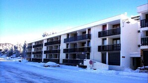 A multi-story building with balconies, a snow-covered street, and a clear sky. - Bright studio with loggia near slopes and shops (Chamrousse)
