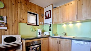 A compact kitchen with wooden cabinets, a microwave, an oven, a sink, and a dishwasher. - Bright apartment near slopes, 2 rooms, West-facing balcony (Chamrousse)
