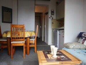 A compact living space with a dining table and chairs, a kitchenette, and a sofa with patterned cushions.