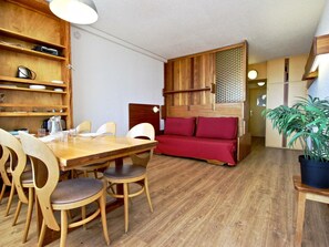A compact living space with a wooden dining table, chairs, a sofa, and a potted plant.