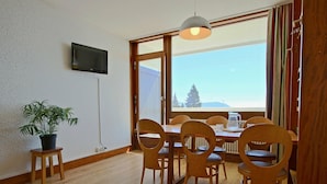 Ein Essbereich mit Holztisch und Stühlen, einer Topfpflanze und einem Fernseher an der Wand.