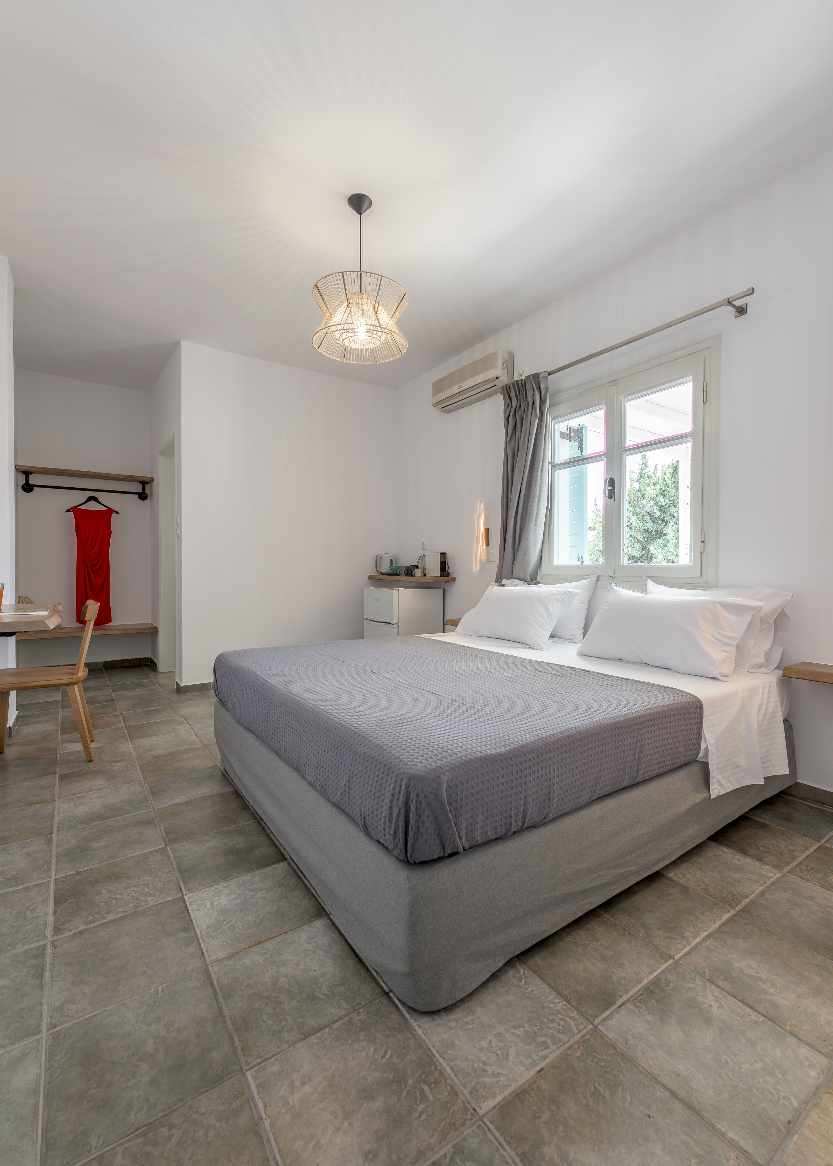 Un dormitorio moderno con una cama grande, un escritorio y una silla. Hay una ventana con cortinas, un equipo de aire acondicionado y una lámpara colgante.