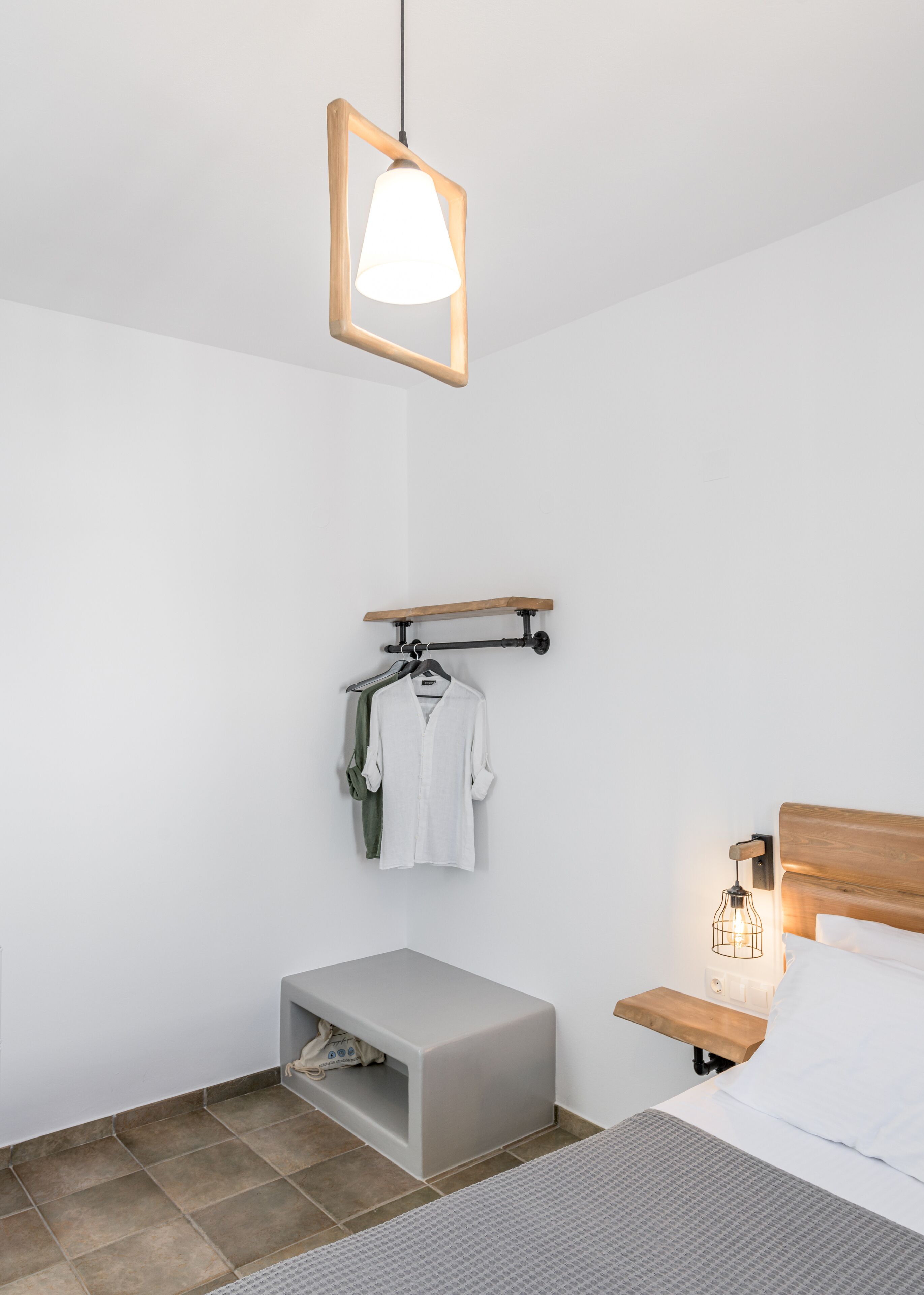A modern bedroom with a bed, bedside table, hanging clothes rack, and a small storage unit.