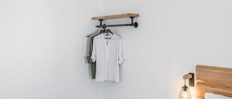 A modern bedroom with a bed, bedside table, hanging clothes rack, and a small storage unit.